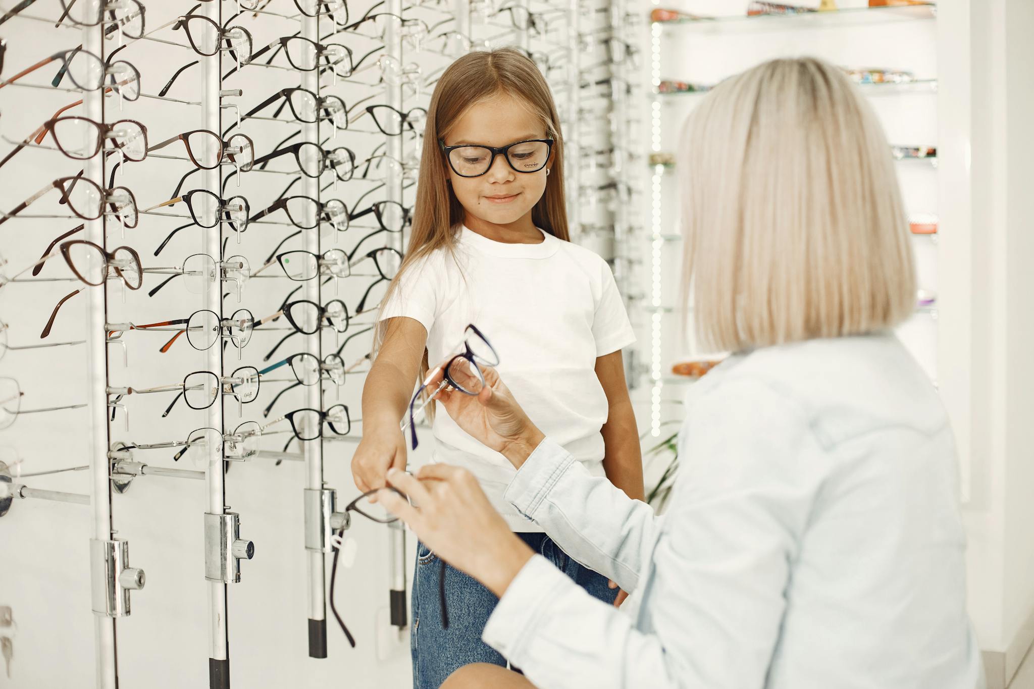A woman helps a child choose glasses in an optical store with a wide selection displayed.